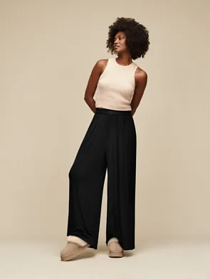 Person in black pants and beige top wearing slippers